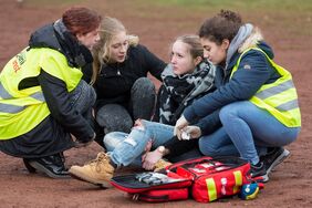 Schulsanitäterinnen helfen einer verunglückten Person auf dem Schulhof